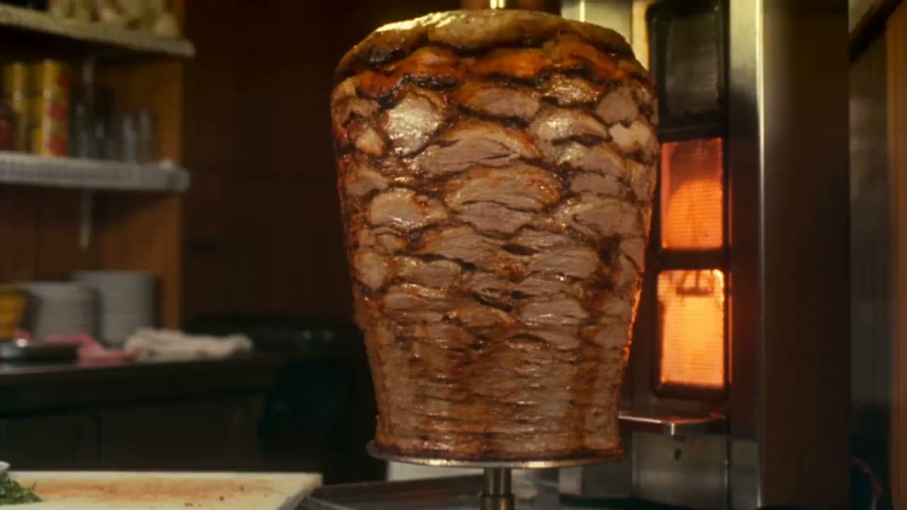 Dönerci tanıtımı: dönen döner, ustanın bıçağı ve sıcak dükkân ışığı. Seedance 2.0 ile üretilen videodan bir kare.
